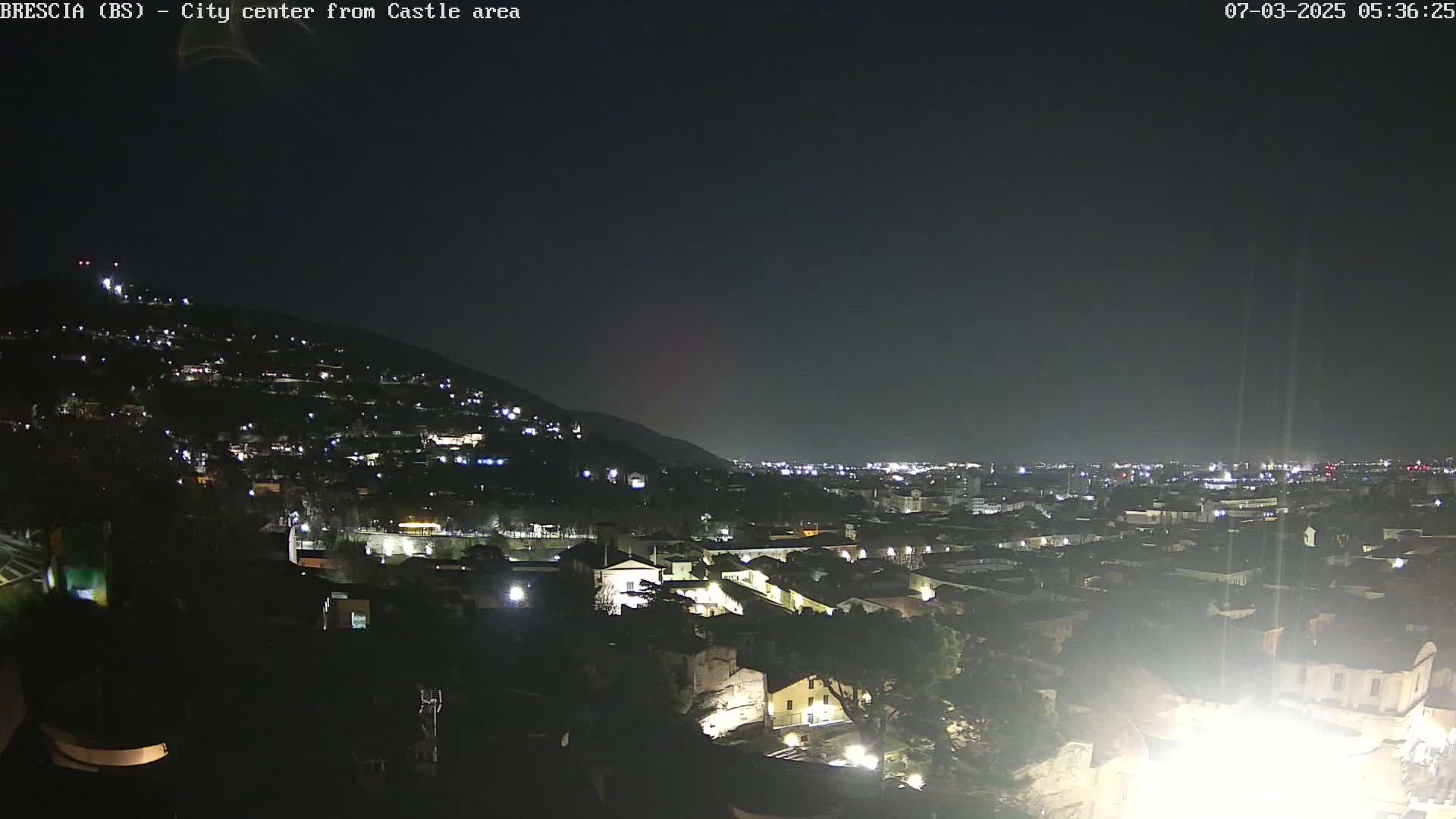 A nighttime view of a city nestled against a hill, illuminated by scattered lights under a dark sky.