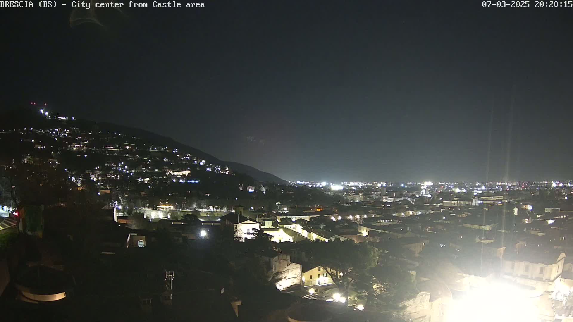 A nighttime view of a city nestled against a hill, illuminated by numerous lights under a clear, dark sky.