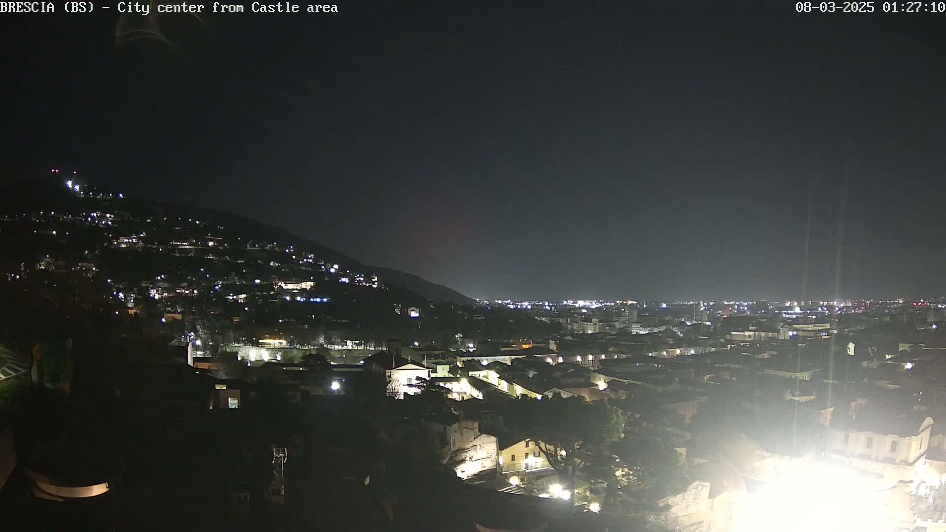 A nighttime view of a city nestled against a hillside, under a clear, dark sky.