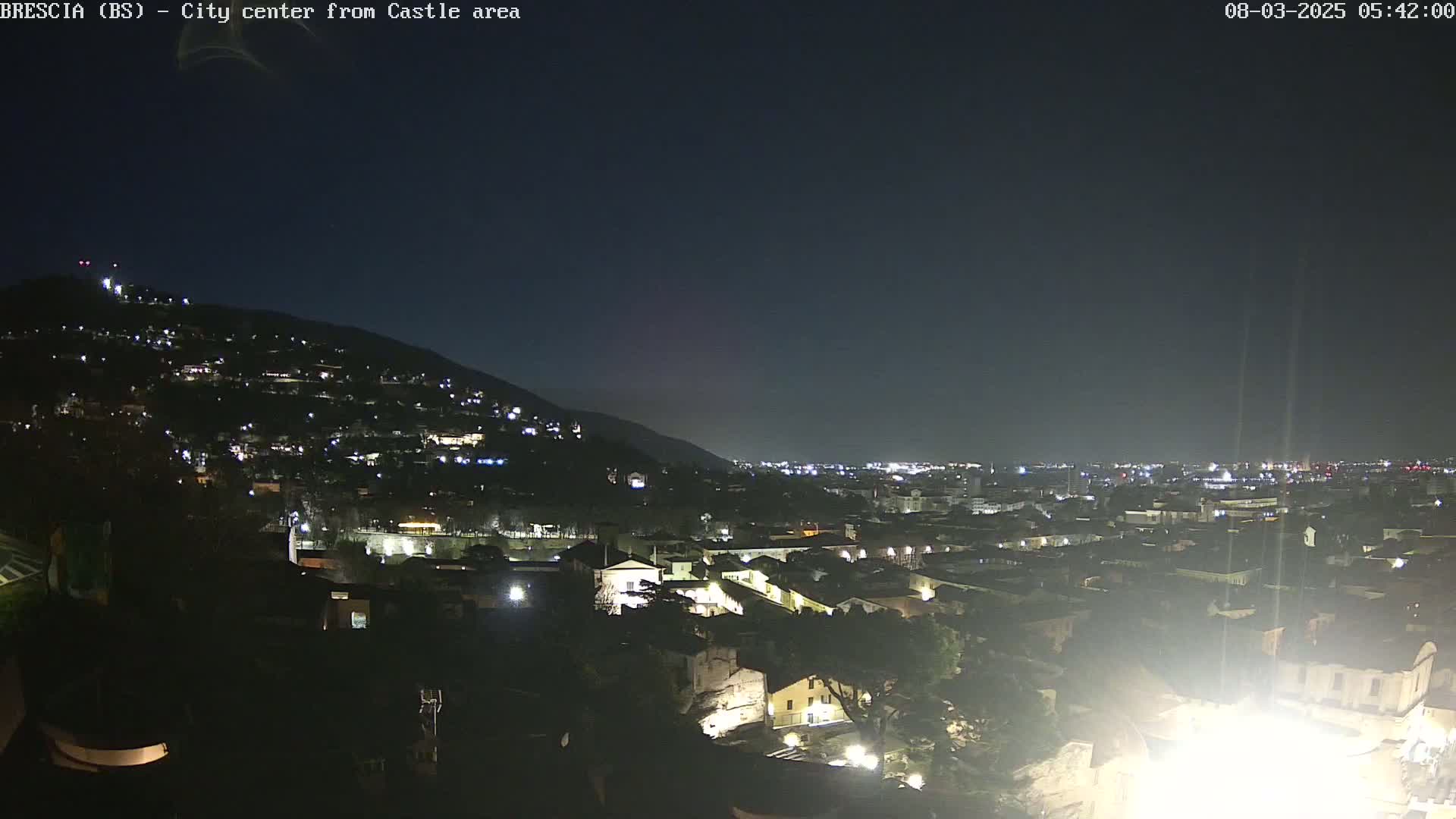 A nighttime view of a city nestled against a hill, with the city lights illuminating the landscape under a clear, dark sky.
