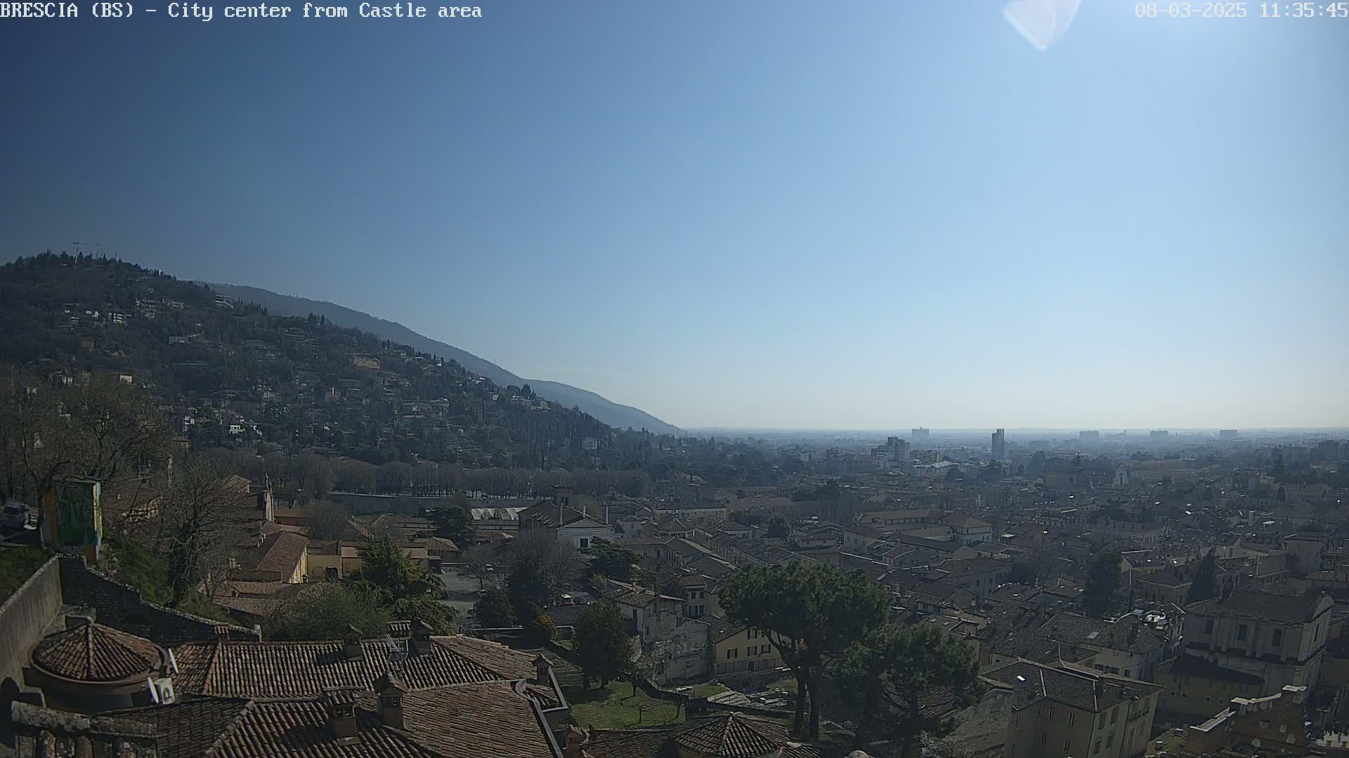 A sprawling city with red-tiled roofs nestles below a hill under a clear, blue sky.