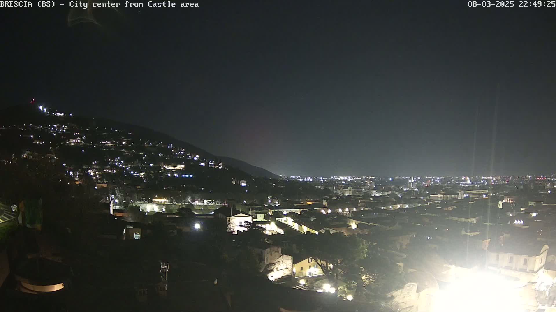 A nighttime view of a city nestled against a hill, illuminated by numerous lights under a dark, clear sky.