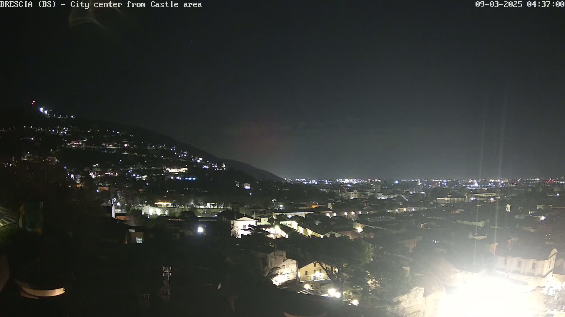 A nighttime view of a city sprawling across a hillside, illuminated by scattered lights under a clear, dark sky.