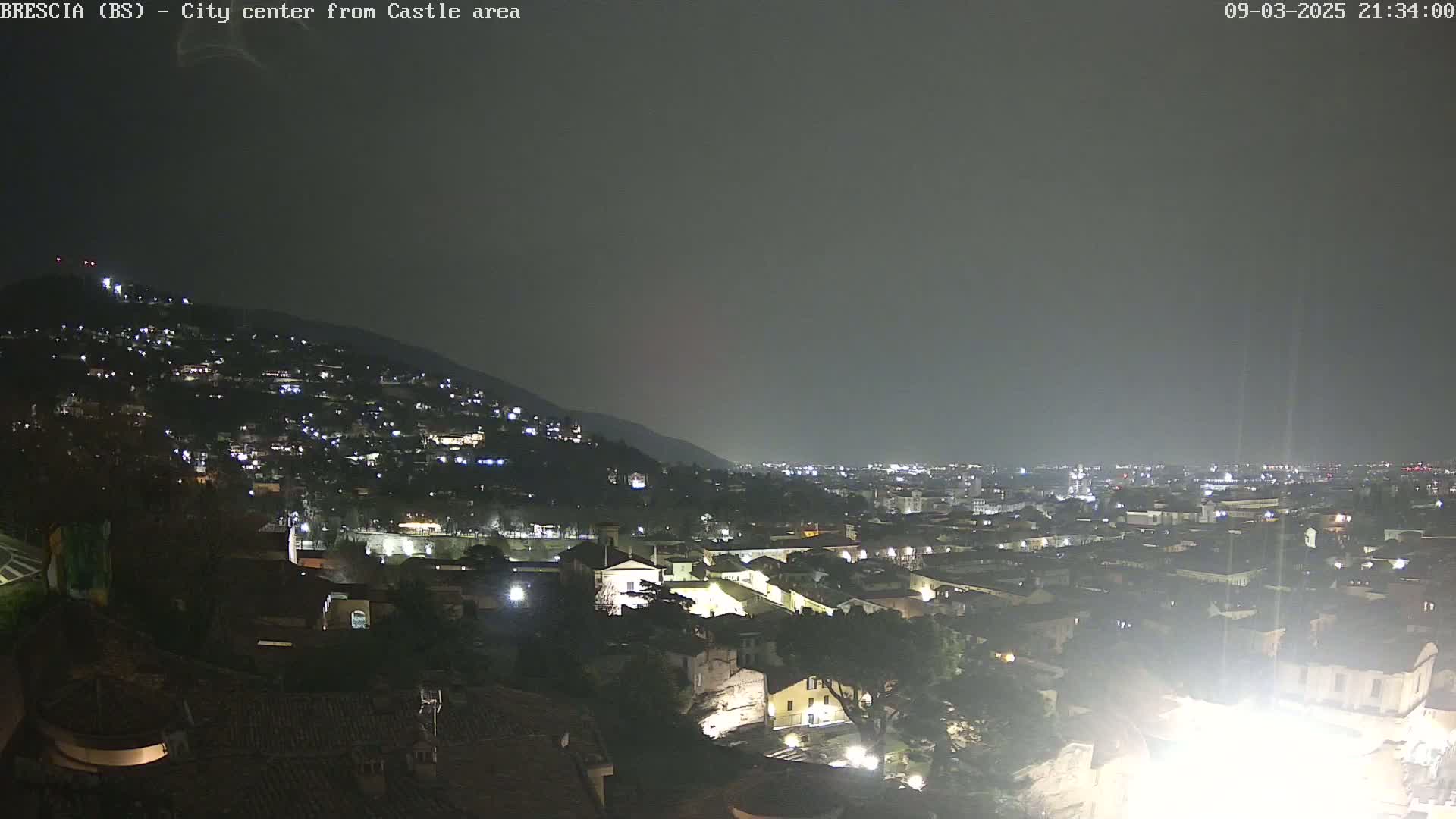 A nighttime view of a city nestled against a hill, under a dark, overcast sky.