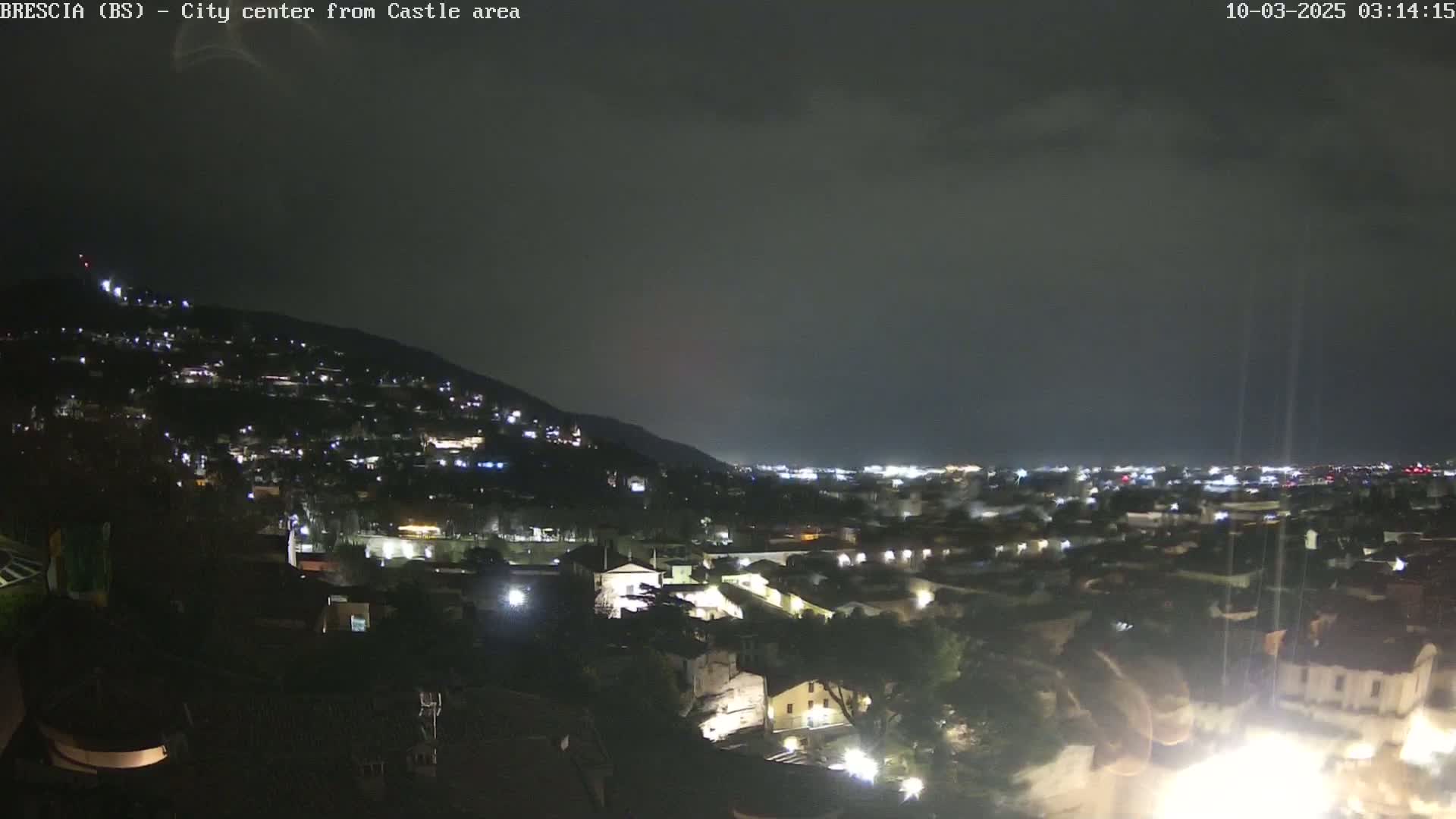 A nighttime view of a city nestled against a hill, under a dark, overcast sky.
