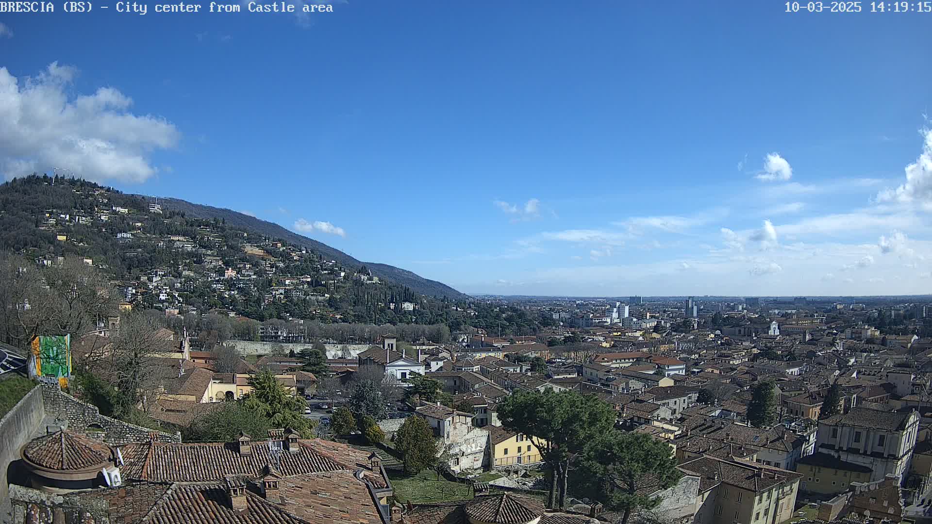 A sprawling city nestled below a mountainside, under a mostly clear blue sky with a few scattered clouds.