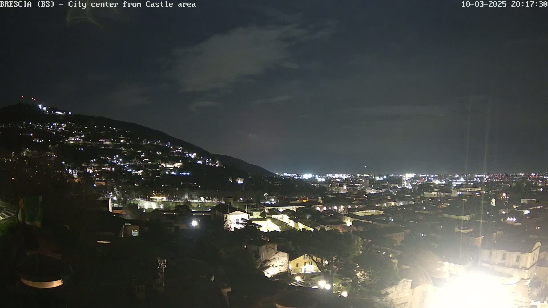 A nighttime view of a city nestled against a hill, under a mostly clear sky.