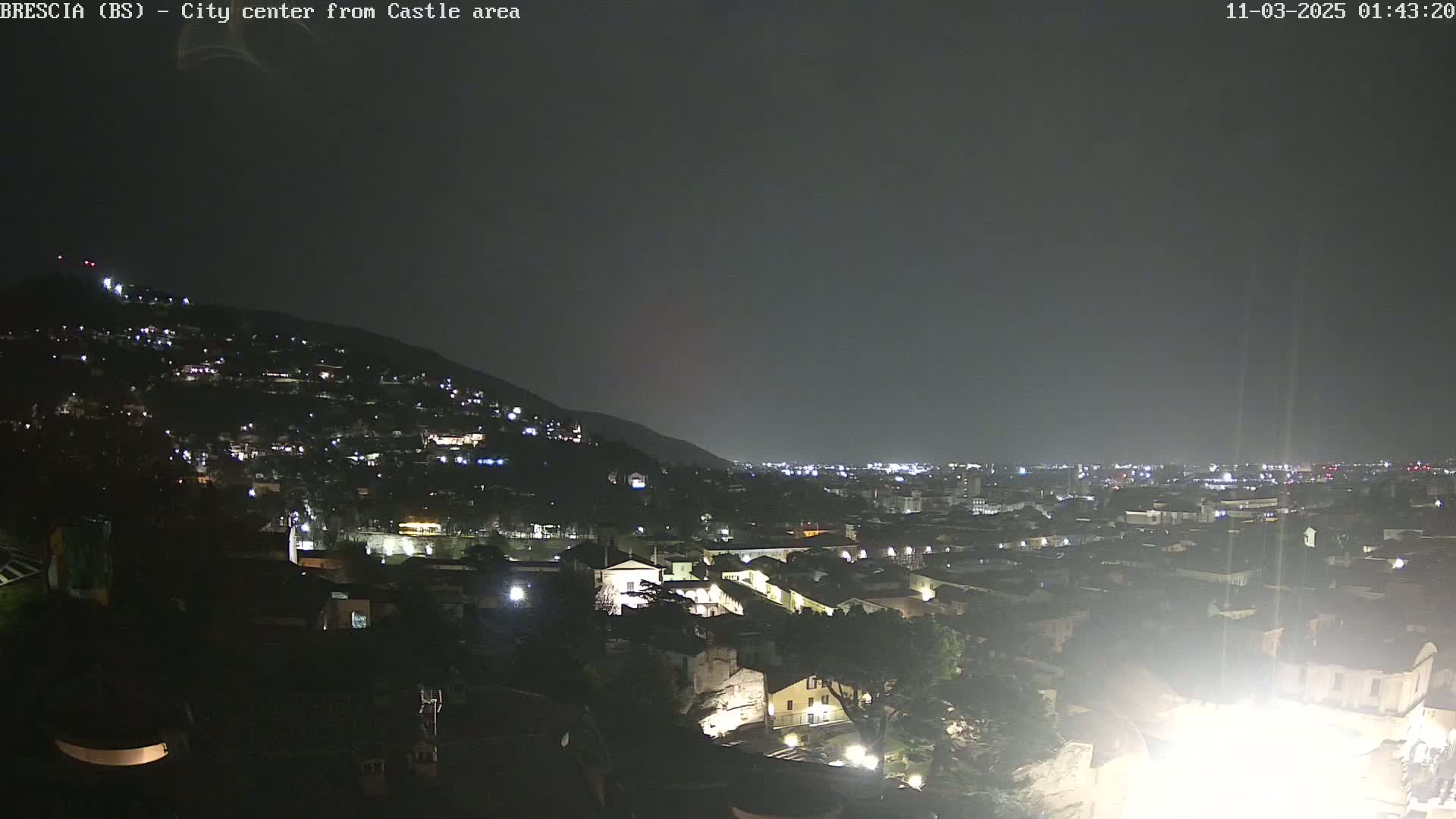 A nighttime view of a city nestled against a hillside, under a dark, overcast sky.
