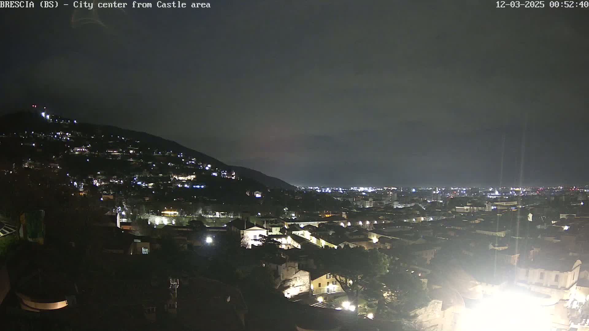 A nighttime view of a city nestled against a hill, under a dark, cloudy sky.