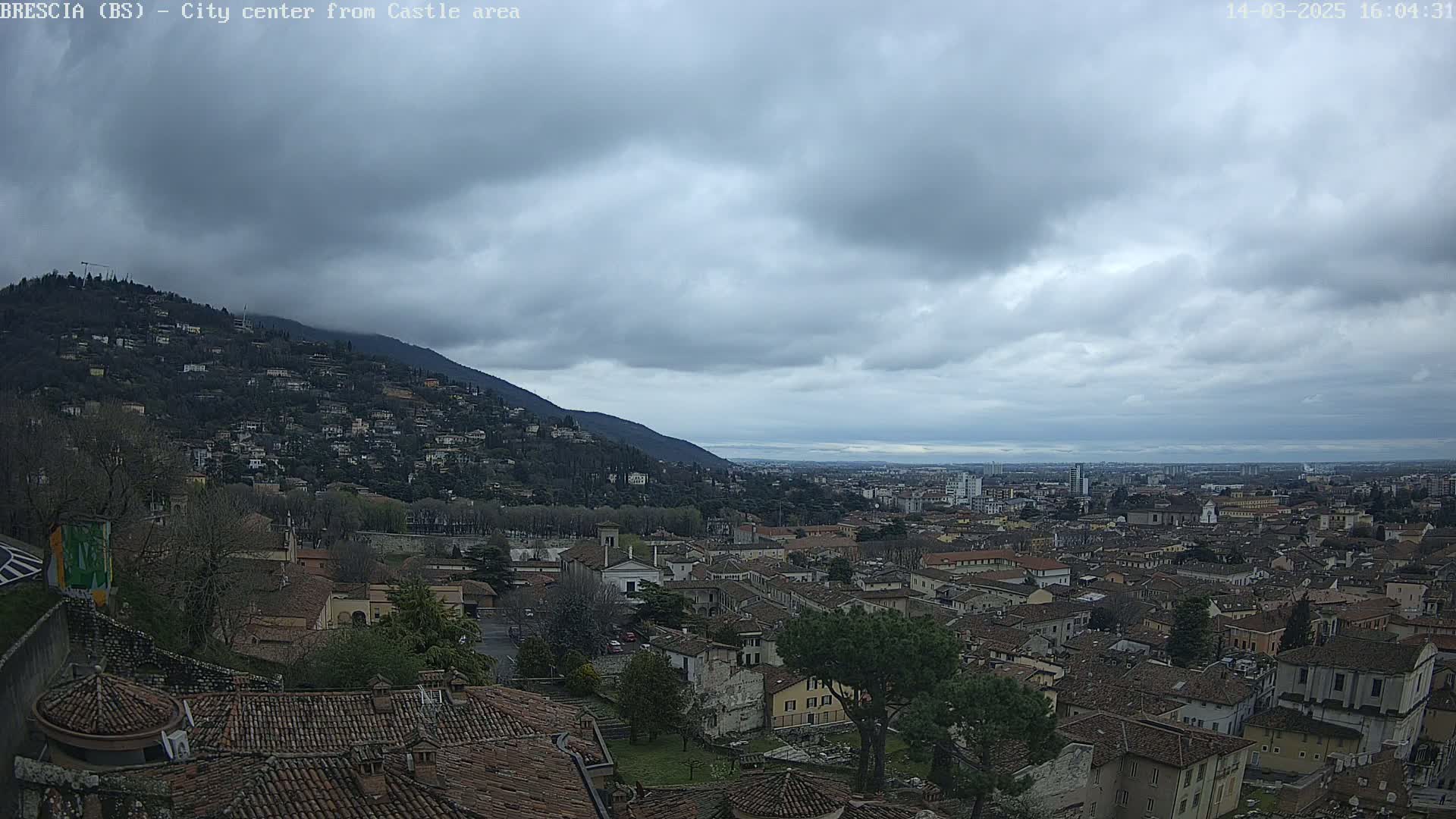 A sprawling city with many low-rise buildings extends to a distant horizon under a cloudy sky.