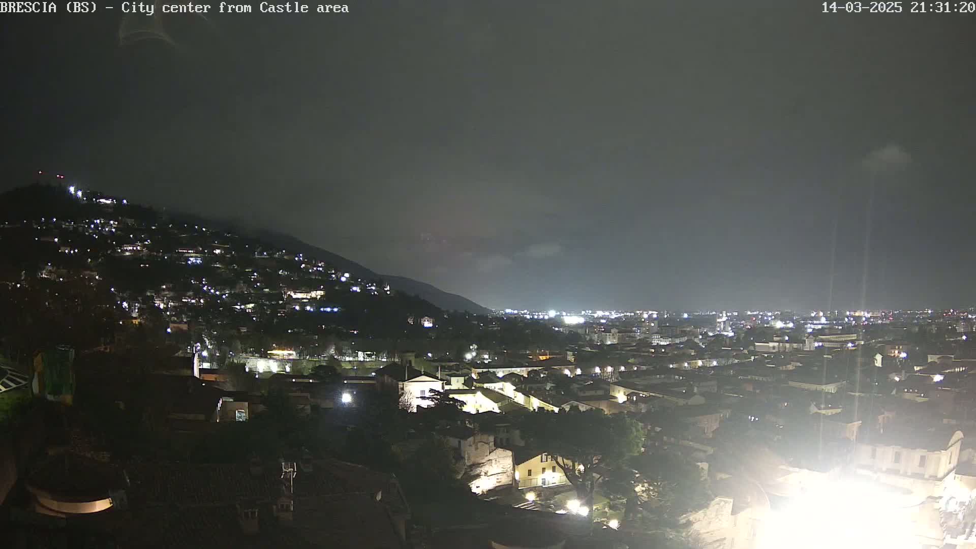 A nighttime view of a city nestled against a hill, under a cloudy sky.