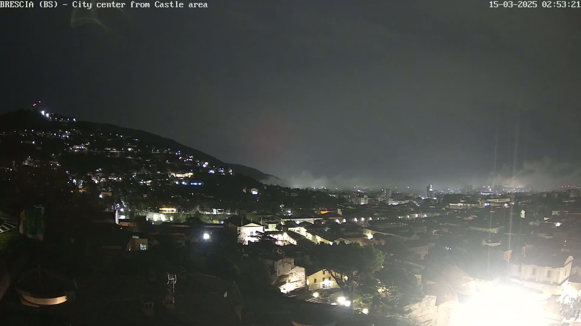 A nighttime view of a city nestled against a hill, under a hazy, dark sky.