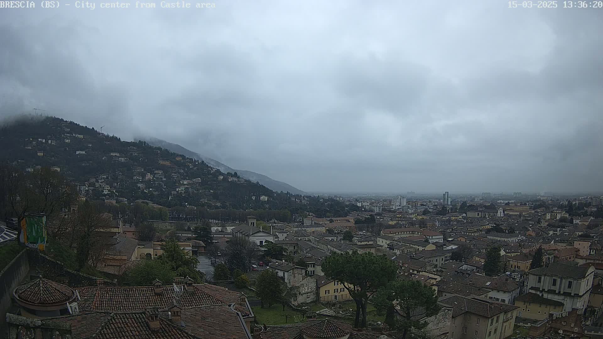 A sprawling city nestled at the foot of a mountain, partially obscured by a cloudy, overcast sky.