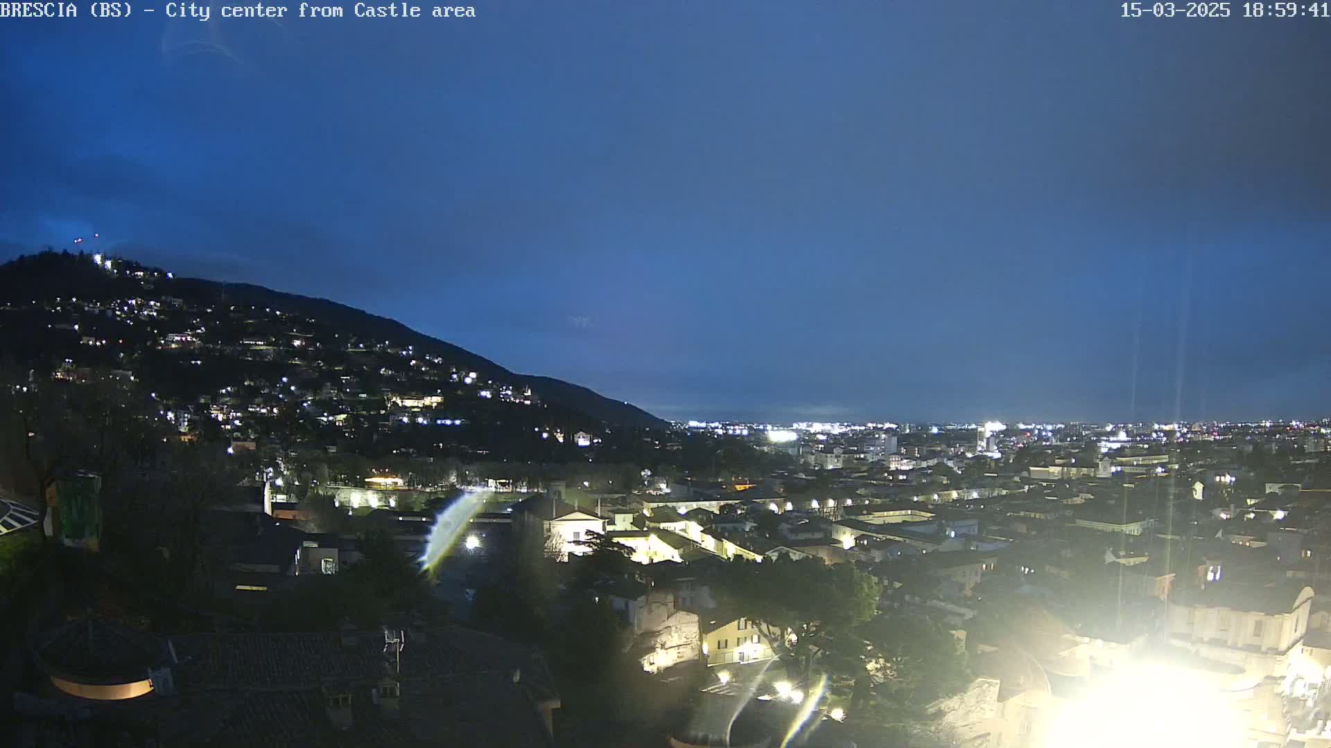 A nighttime view of a city nestled at the base of a hill, under a clear, dark blue sky.