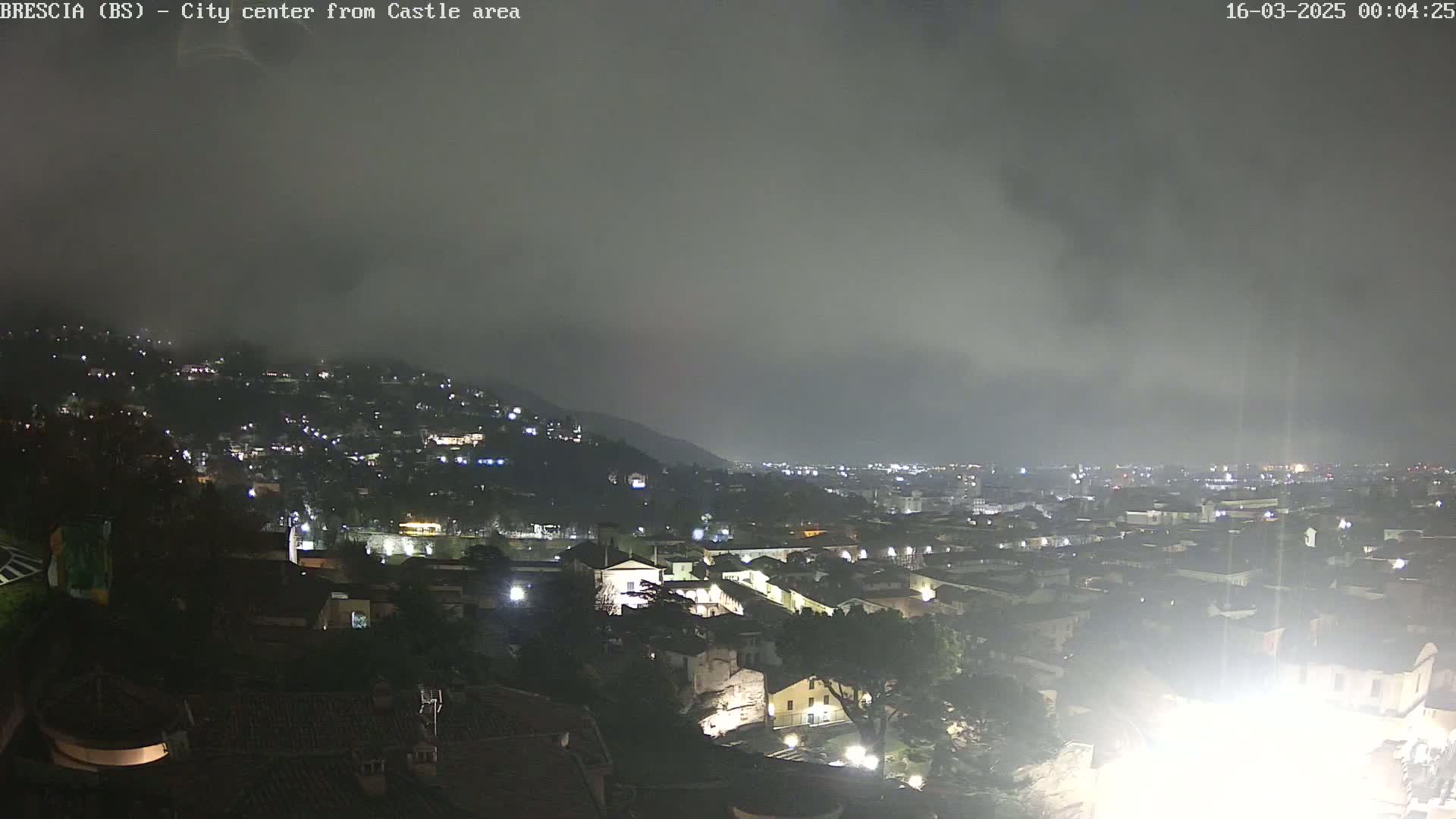 A nighttime view of a city nestled in a valley under a hazy, overcast sky.