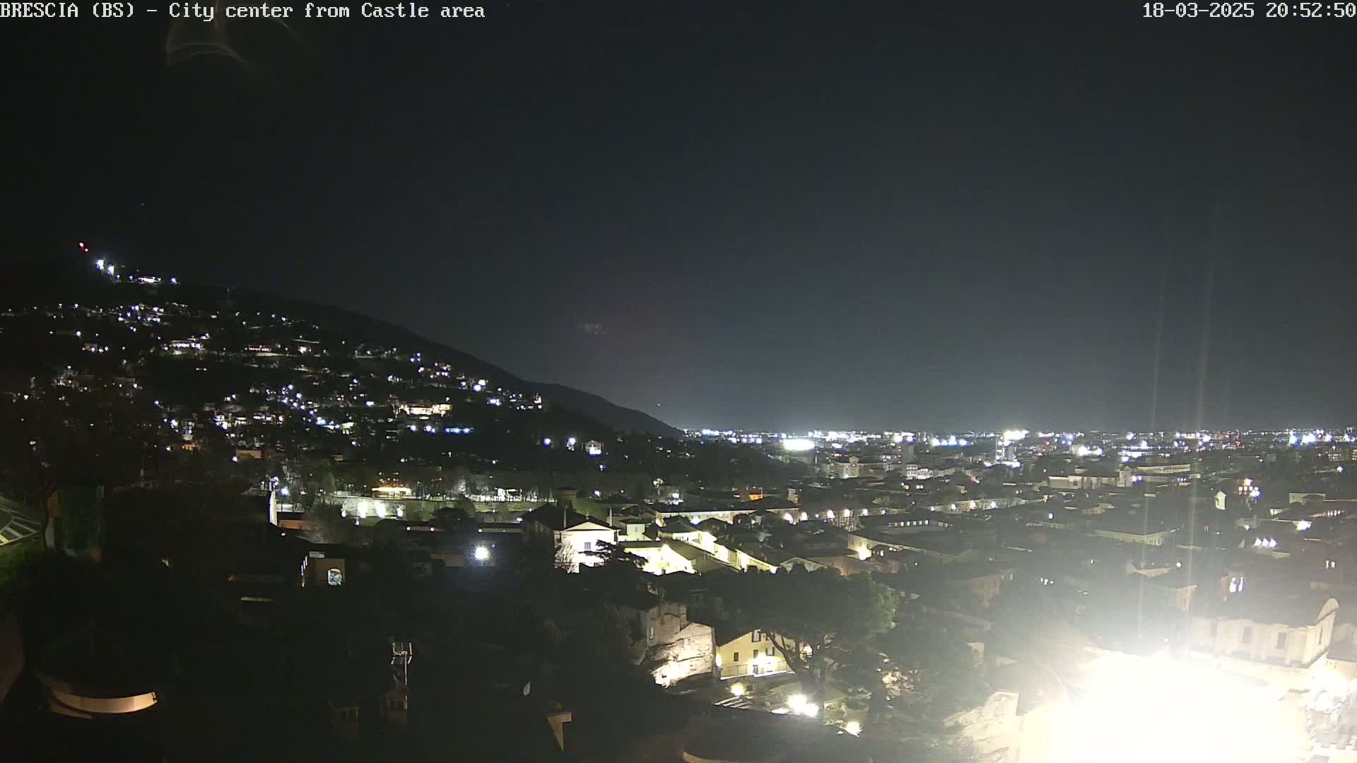 A nighttime view of a city nestled against a hillside, illuminated by numerous lights under a clear, dark sky.
