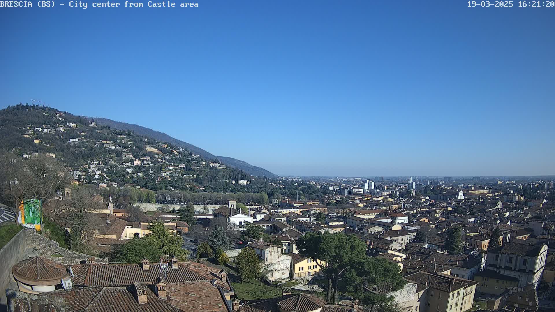 A sprawling city nestled against a hillside under a clear blue sky.
