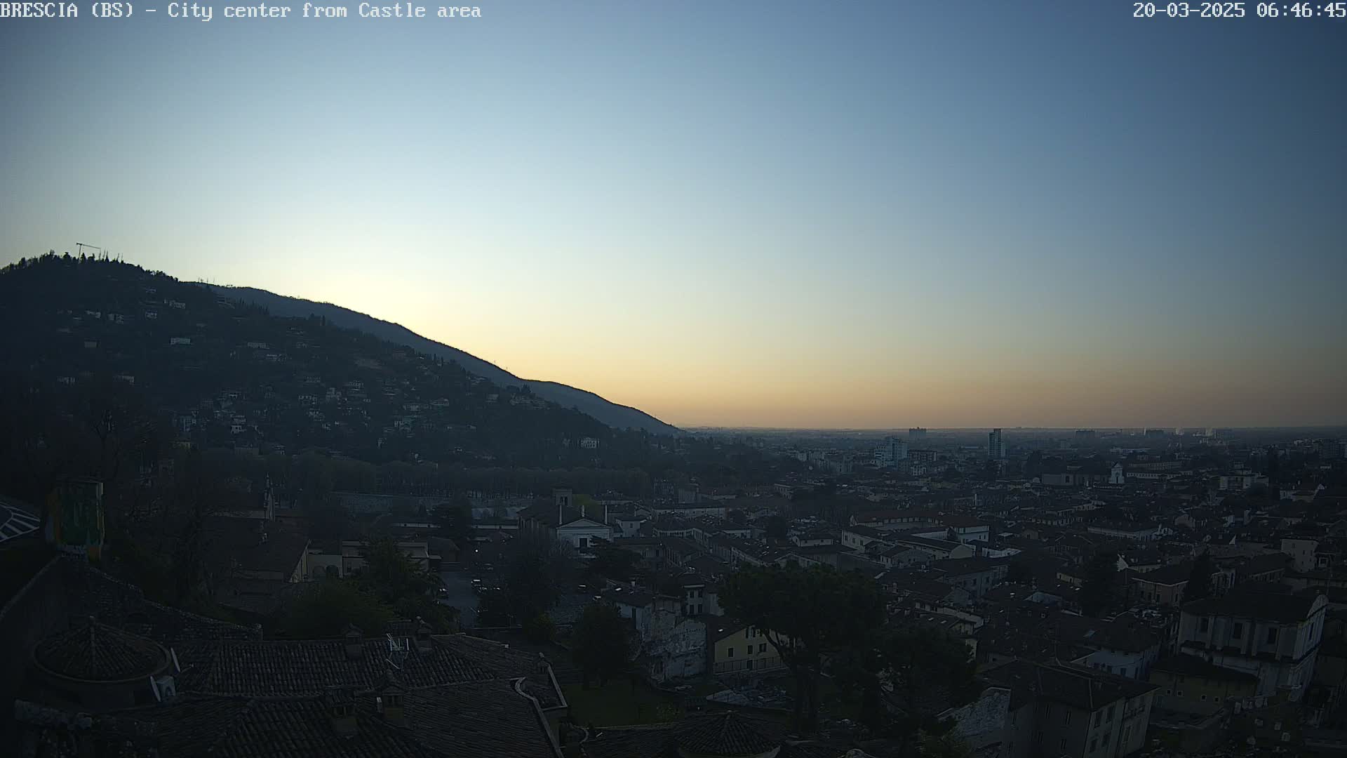 A city sprawls below a hill at sunrise under a clear, dusky sky.