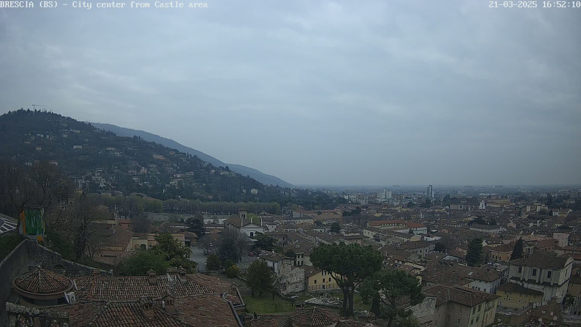 A view of a city nestled in a valley beneath a hill, on an overcast day.