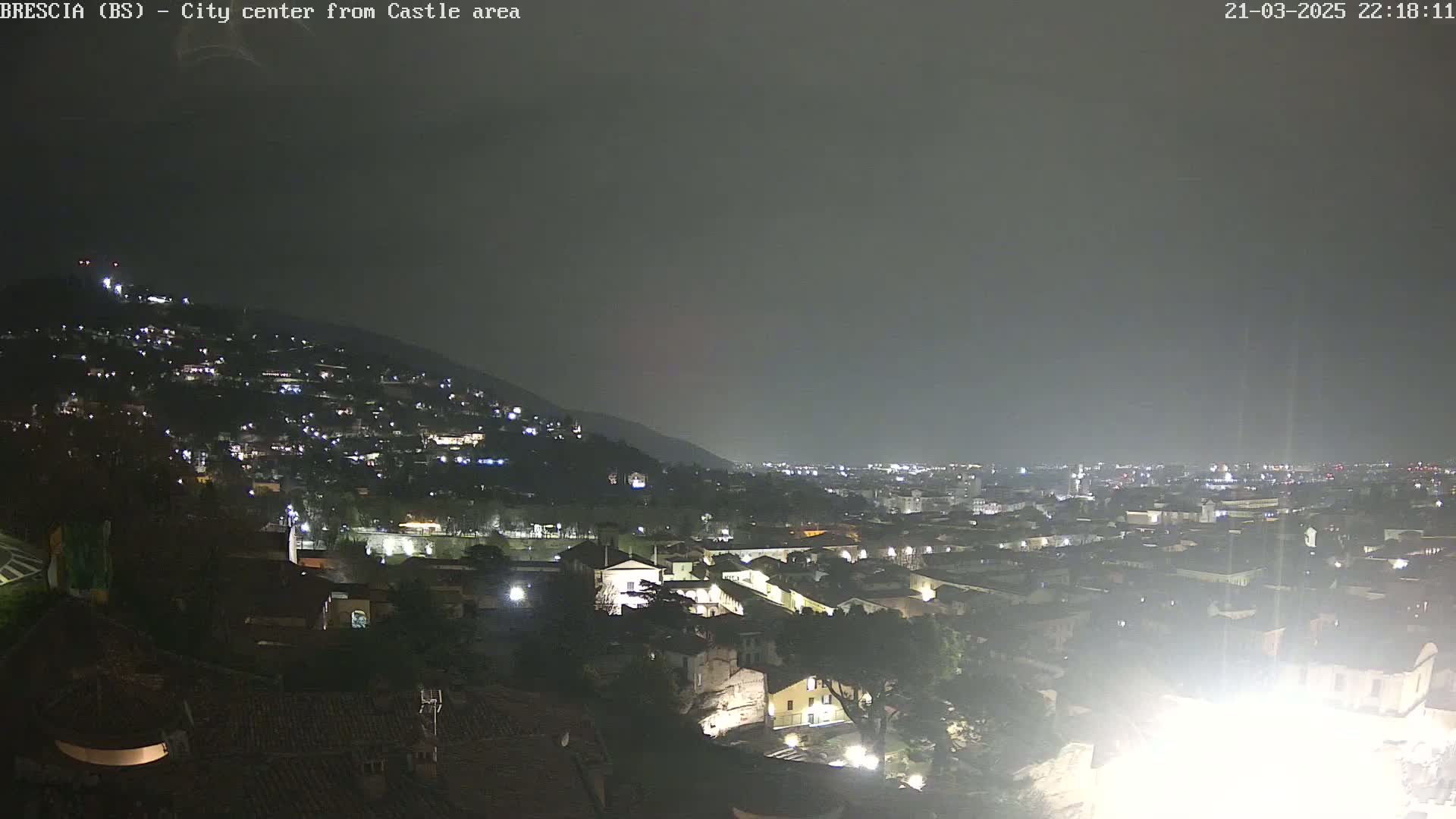 A nighttime, wide shot shows a city sprawling across a hillside under a dark, overcast sky.