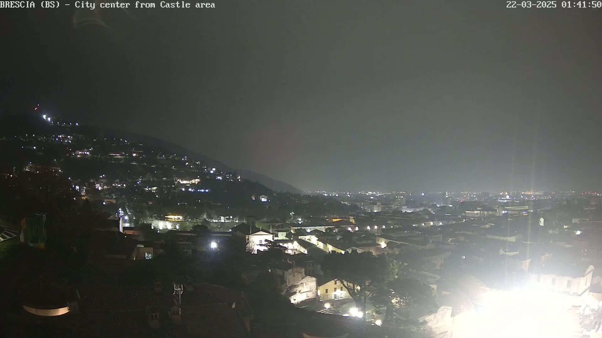 A nighttime view of a city nestled against a hill, under a hazy, dark sky.
