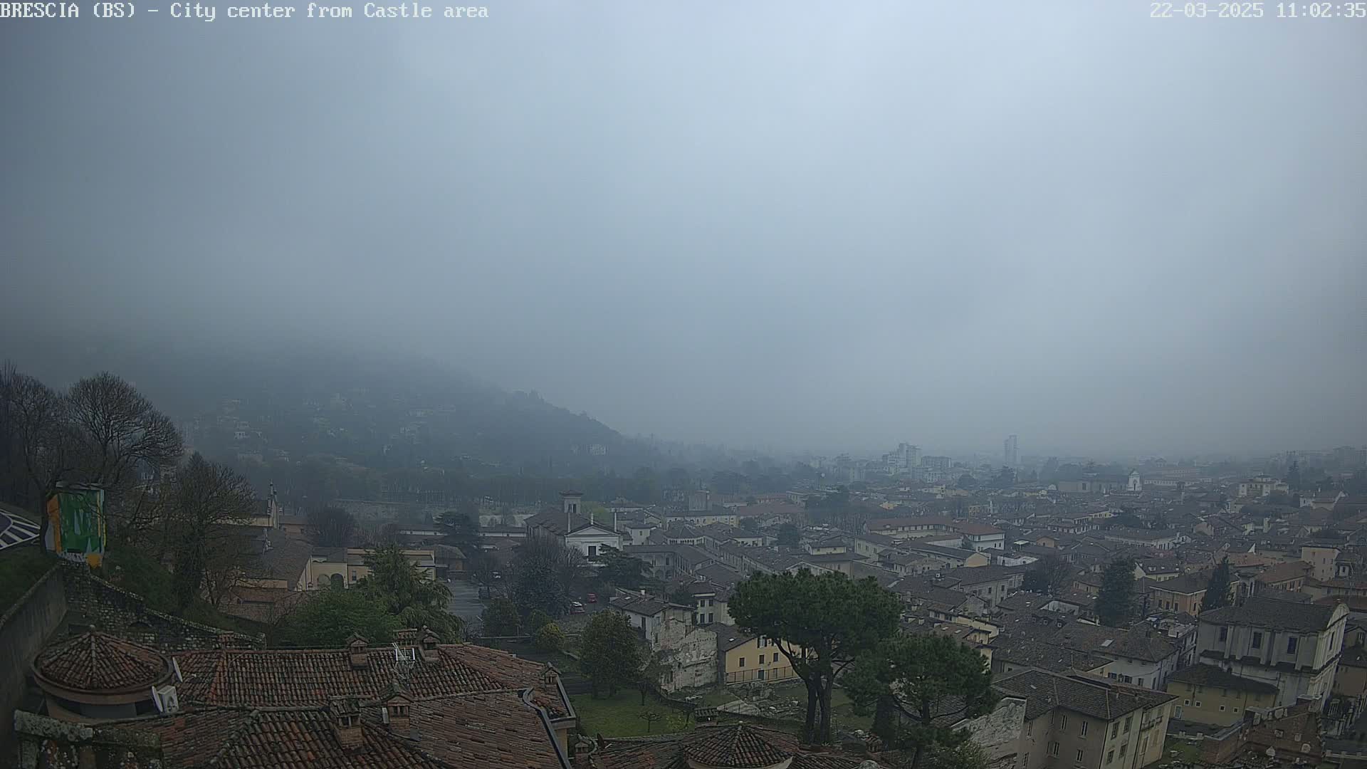 A foggy view of a city sprawling across a valley, seen from a high vantage point with terracotta rooftops visible in the foreground.