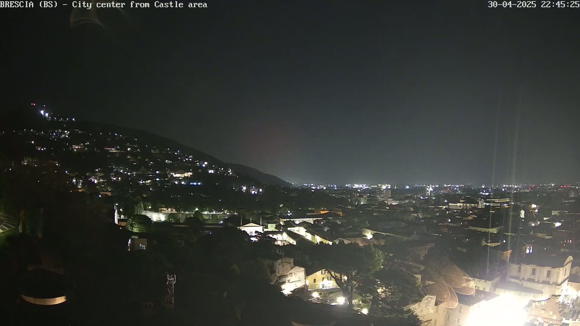 A nighttime view of a city nestled against a hill, illuminated by scattered lights under a clear, dark sky.