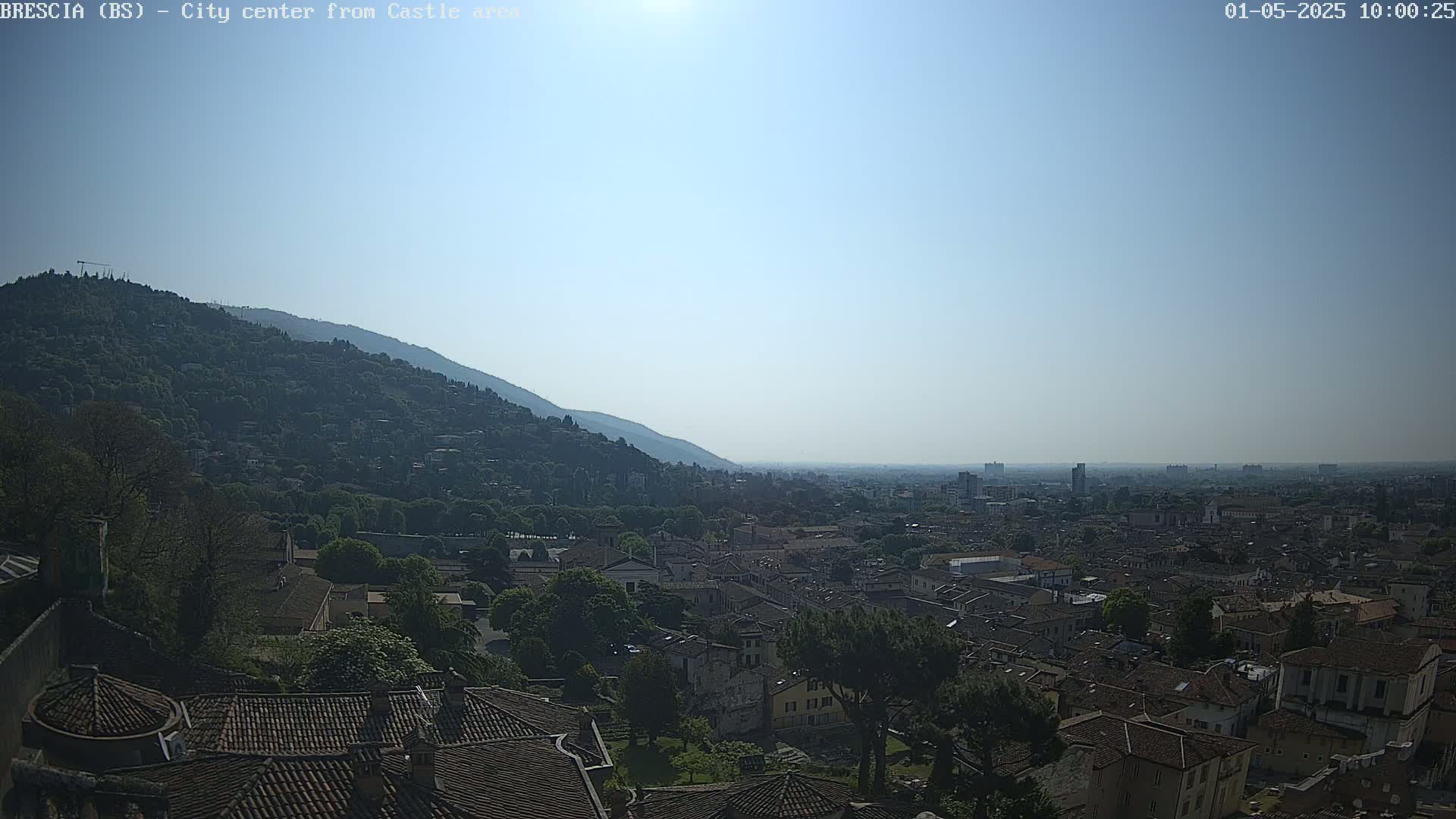 A sunny view shows a city nestled between a hillside and a hazy plain, with many brown-roofed buildings visible from a high vantage point.