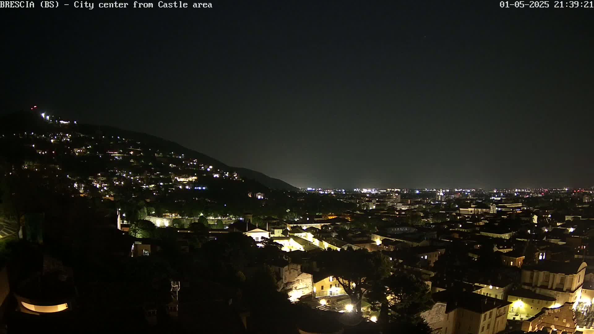A nighttime view of a city nestled in a valley, illuminated by numerous lights, under a dark, clear sky.