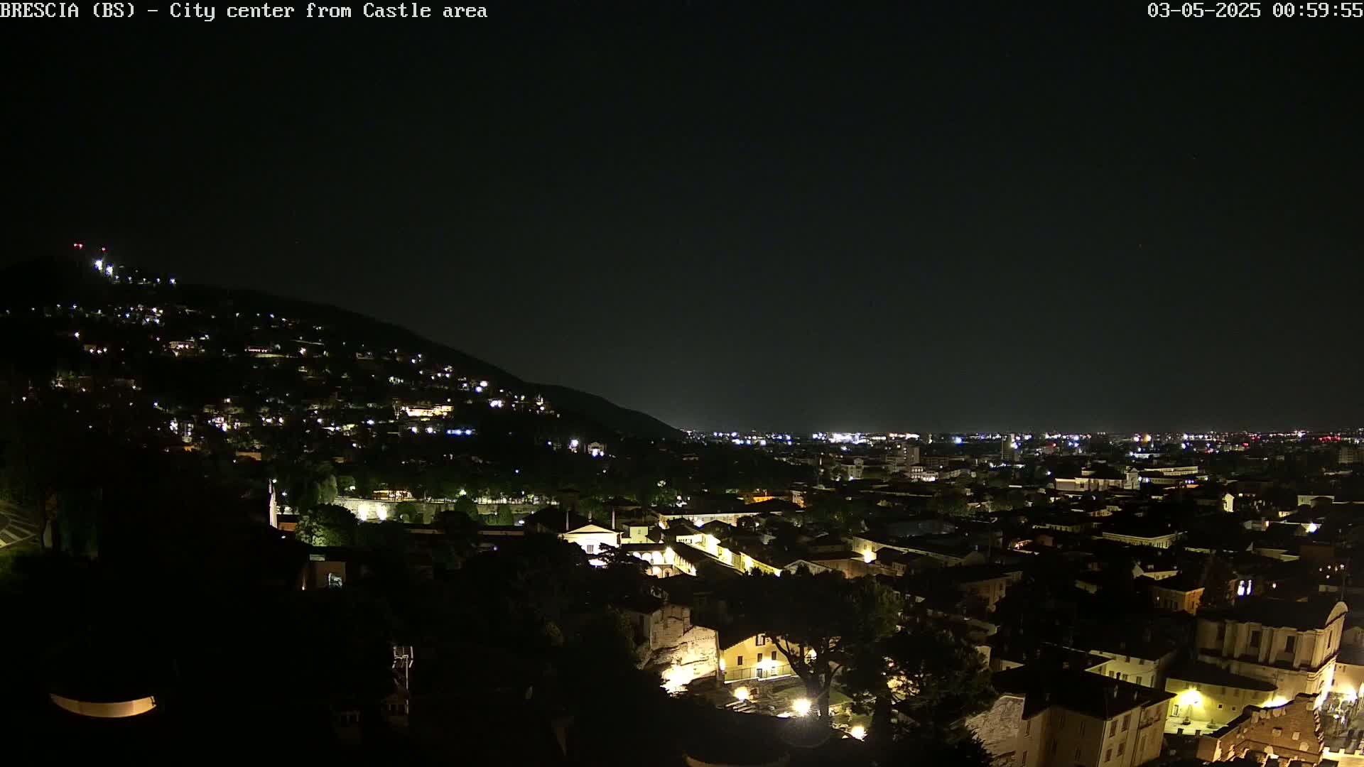 A nighttime view of a city nestled against a hill, illuminated by scattered lights under a clear, dark sky.