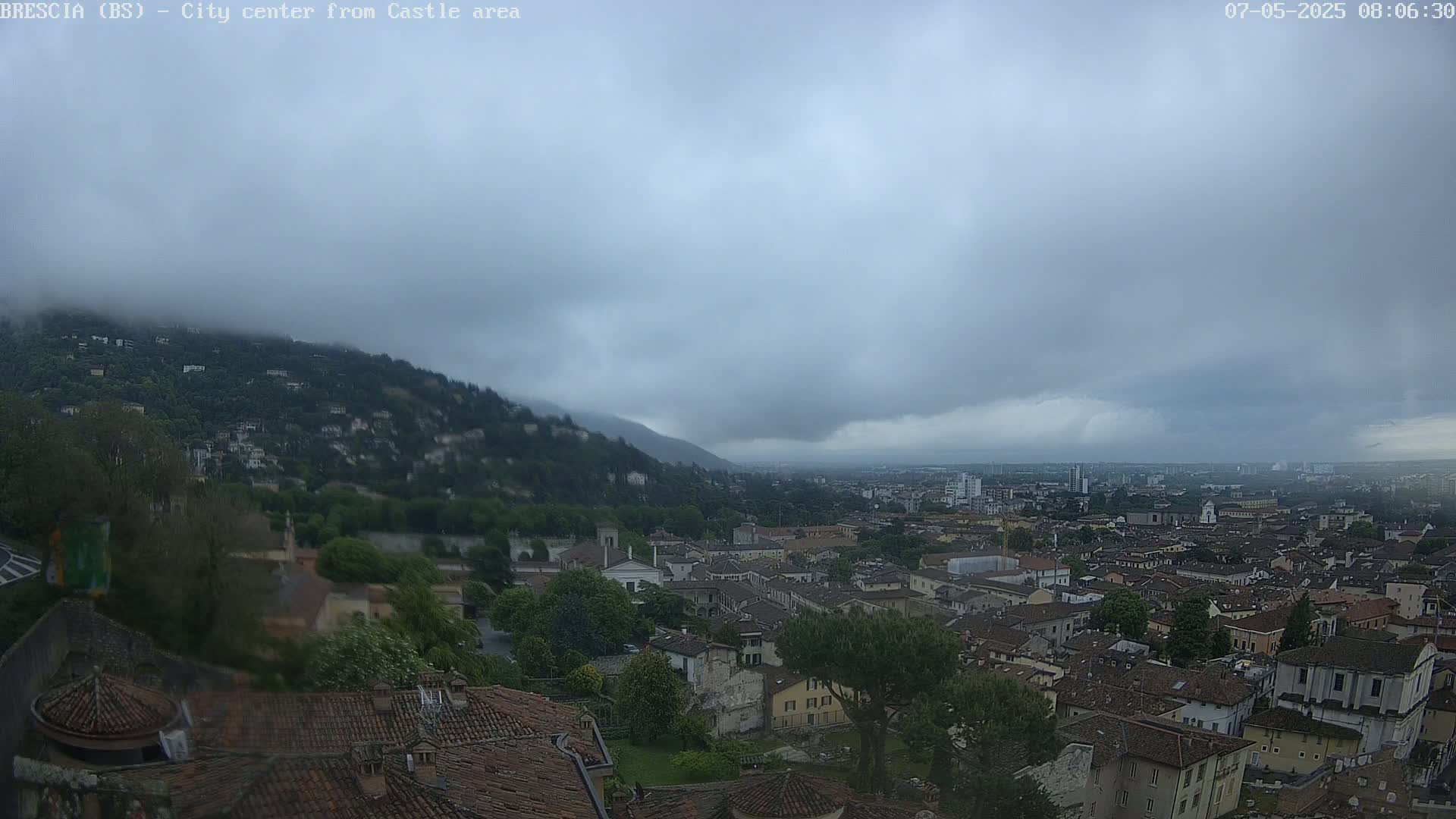 A city nestled in a valley beneath a hill shrouded in fog, under an overcast sky.