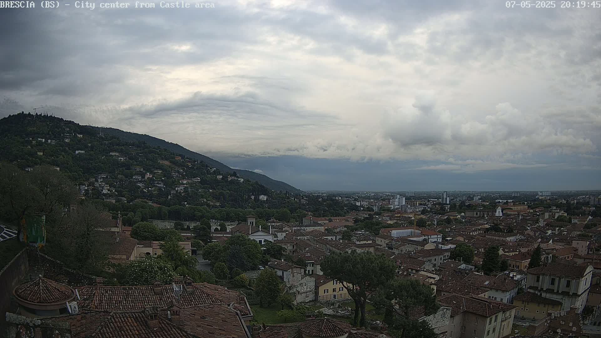 A sprawling city with red-tiled roofs nestled against a hill under a cloudy sky.