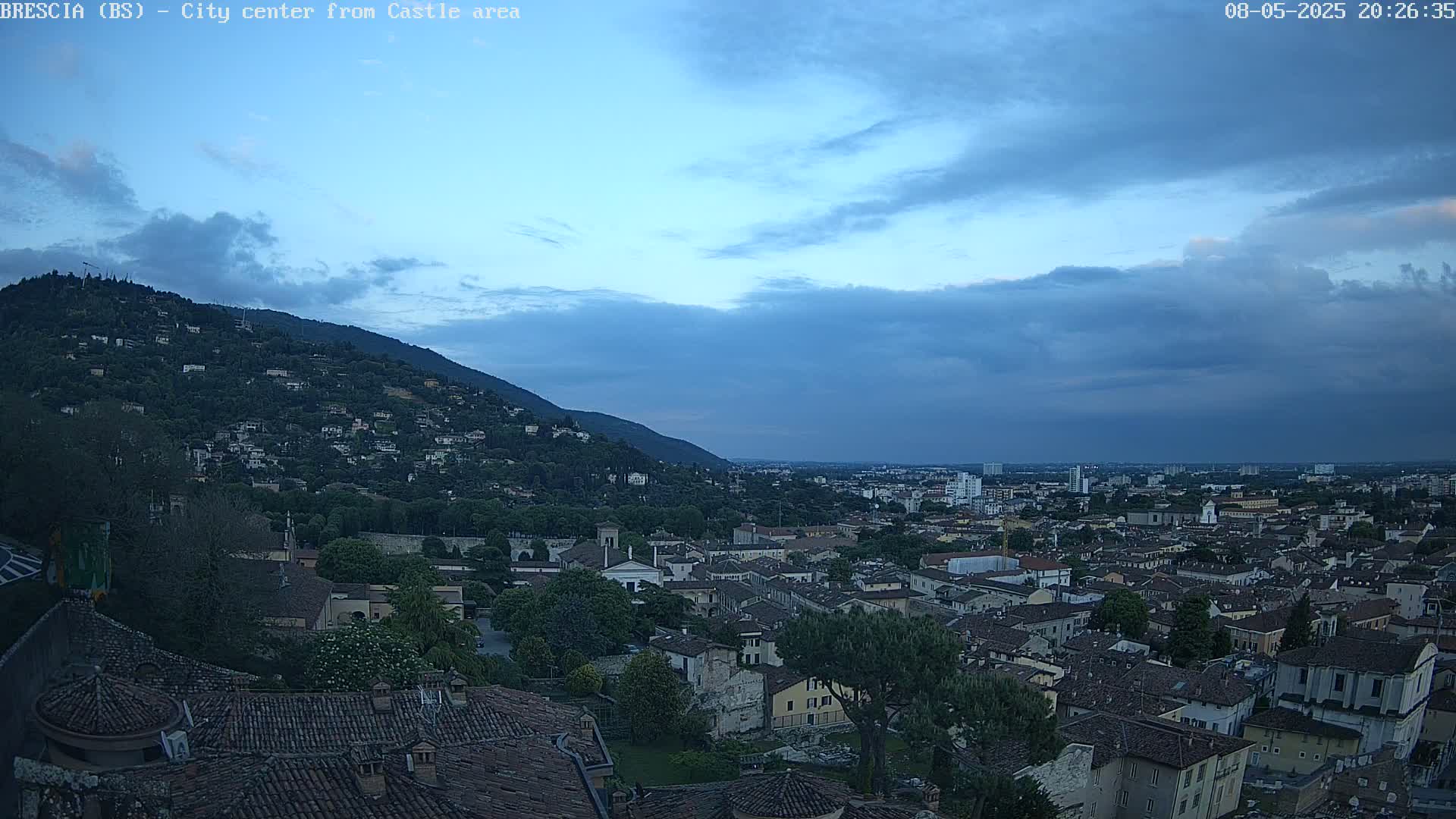A sprawling city, nestled beneath a hill and a cloudy, twilight sky.