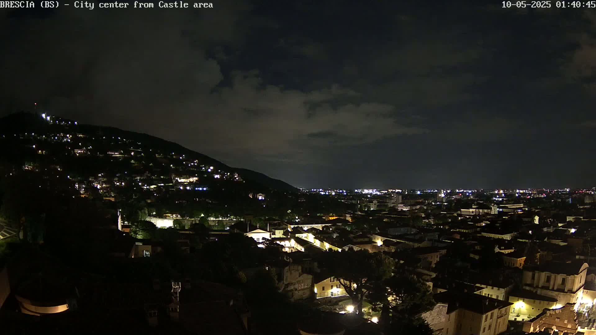 A nighttime view of a city nestled at the base of a hill, under a partly cloudy sky.