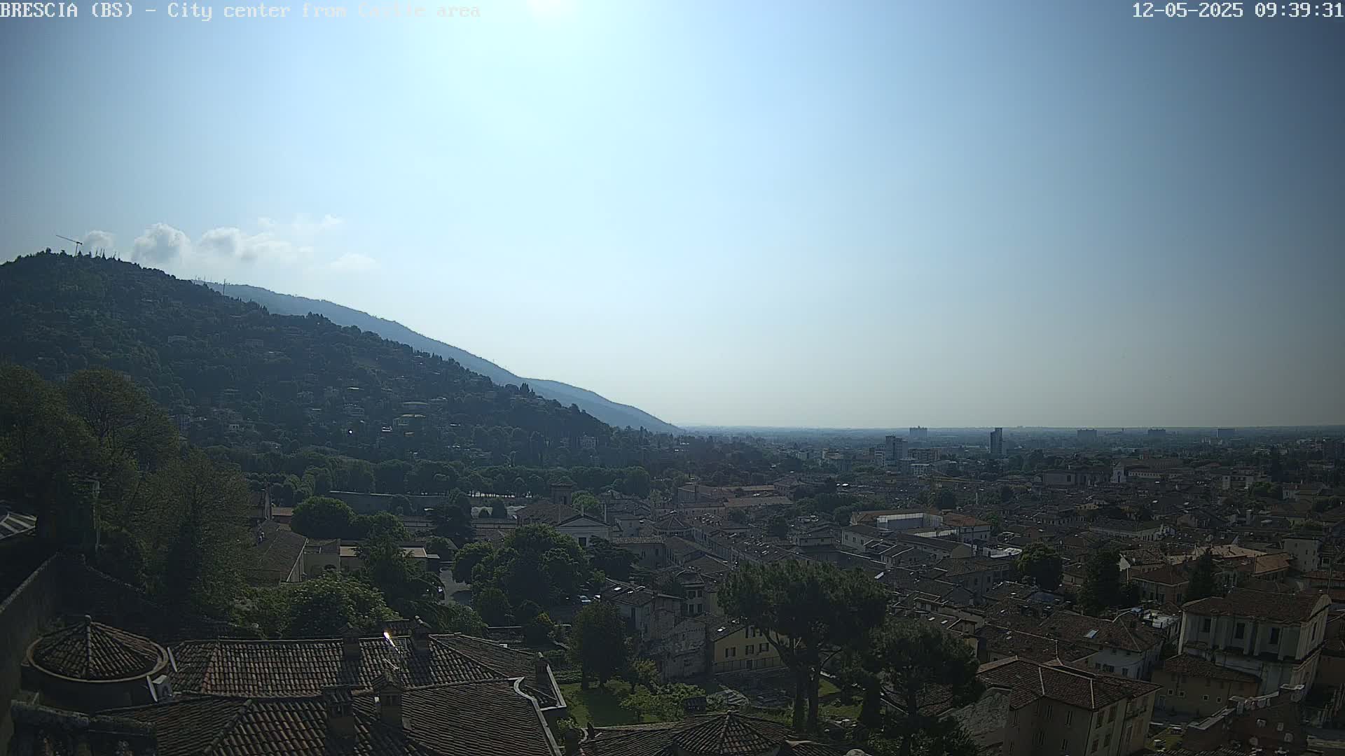 A sunny view overlooking a city nestled against a mountainside, with many low buildings and rooftops visible.