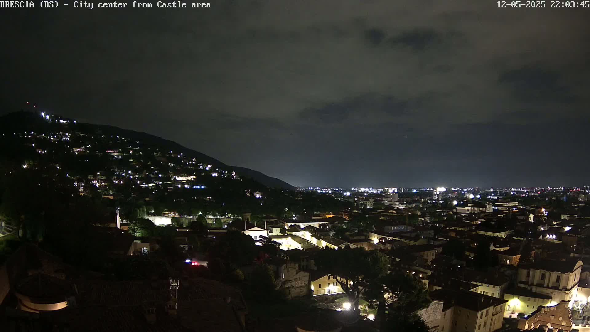 A nighttime view of a city sprawling across a hill and plain under a dark, cloudy sky.
