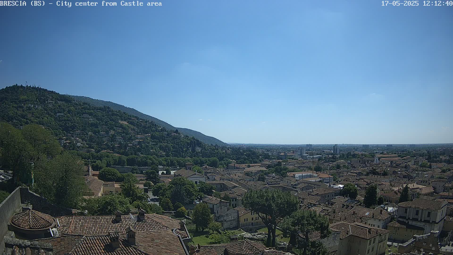 A sprawling city with terracotta rooftops nestled beneath a clear blue sky and a verdant hillside.