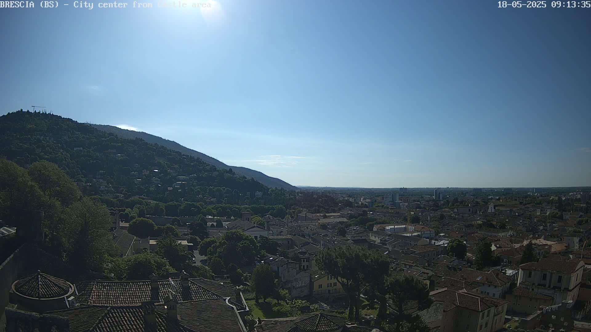 A sunny day reveals a sprawling city nestled against a verdant hillside, extending to a distant horizon.