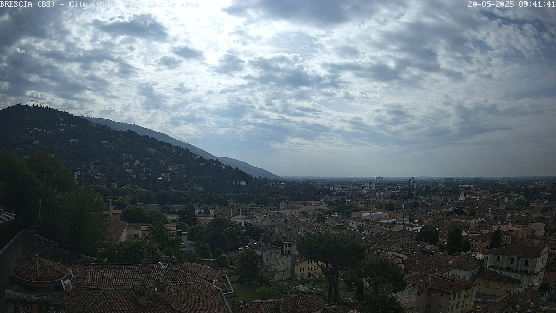 A sprawling city nestled beneath a cloudy sky, with a mountain rising in the background.