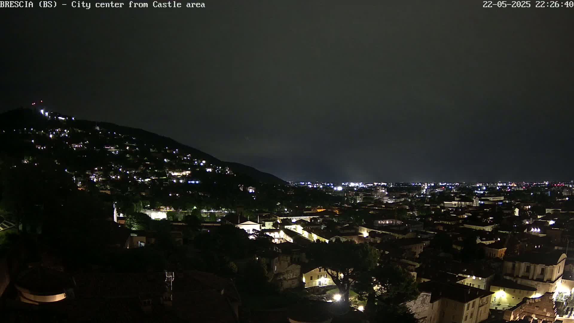 A nighttime view of a city nestled against a hillside, under a dark, overcast sky.