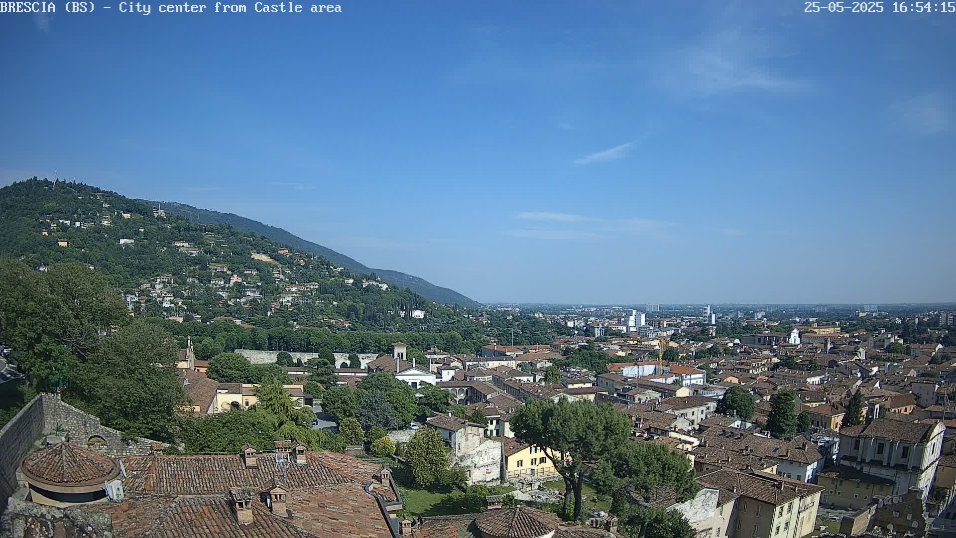 A sprawling city with terracotta rooftops extends from a hilltop, under a mostly clear blue sky.