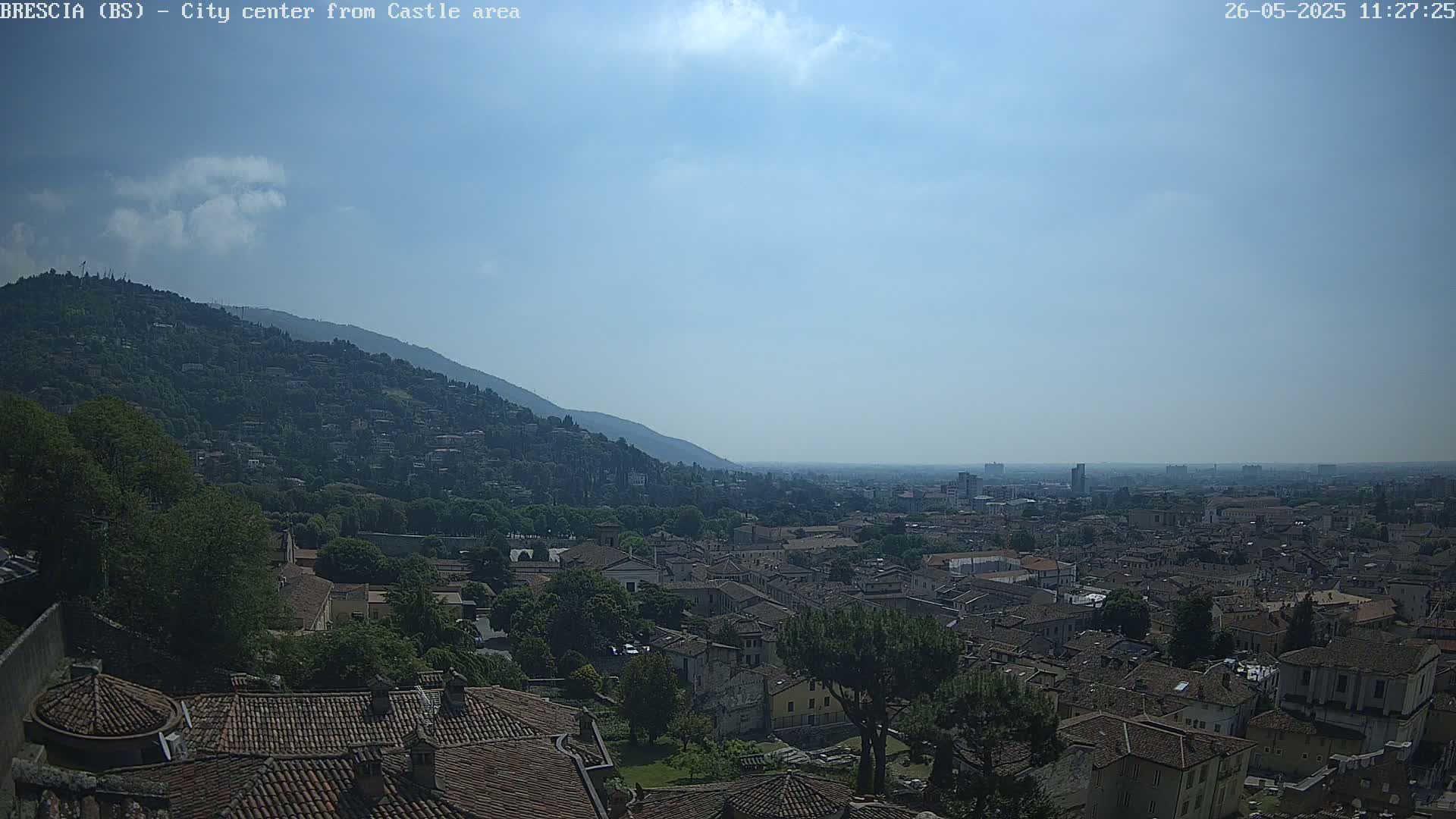 A sprawling city with terracotta rooftops extends from a hill into a hazy distance under a mostly sunny sky.