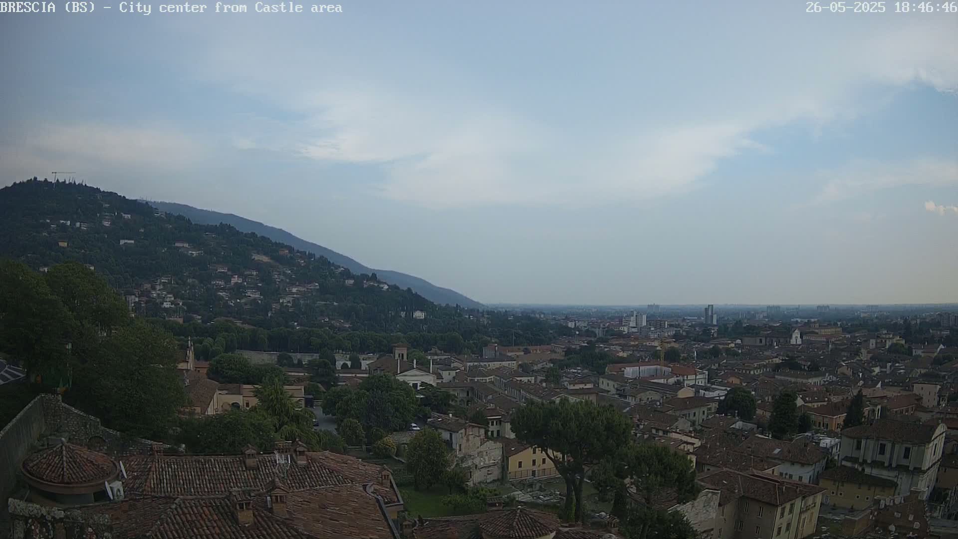 A sprawling city with red-tiled roofs extends from a hilltop, under a mostly clear, light-blue sky.
