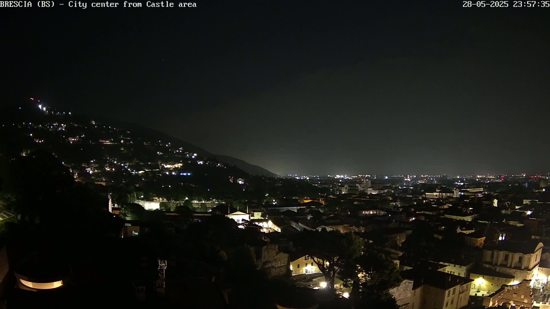 A nighttime view of a city nestled at the base of a hill, with numerous lights illuminating buildings and streets under a clear, dark sky.