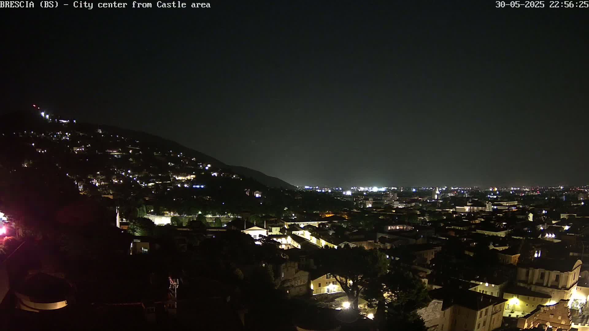 A nighttime view of a city nestled in a valley, illuminated by scattered lights against a dark sky.