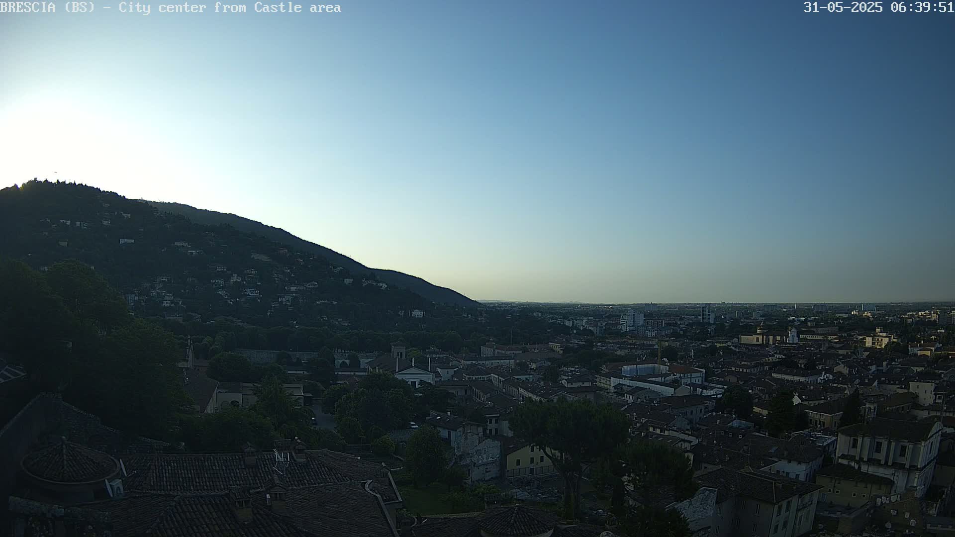 A sprawling city nestled beneath a hill, viewed at dawn under a clear, blue sky.