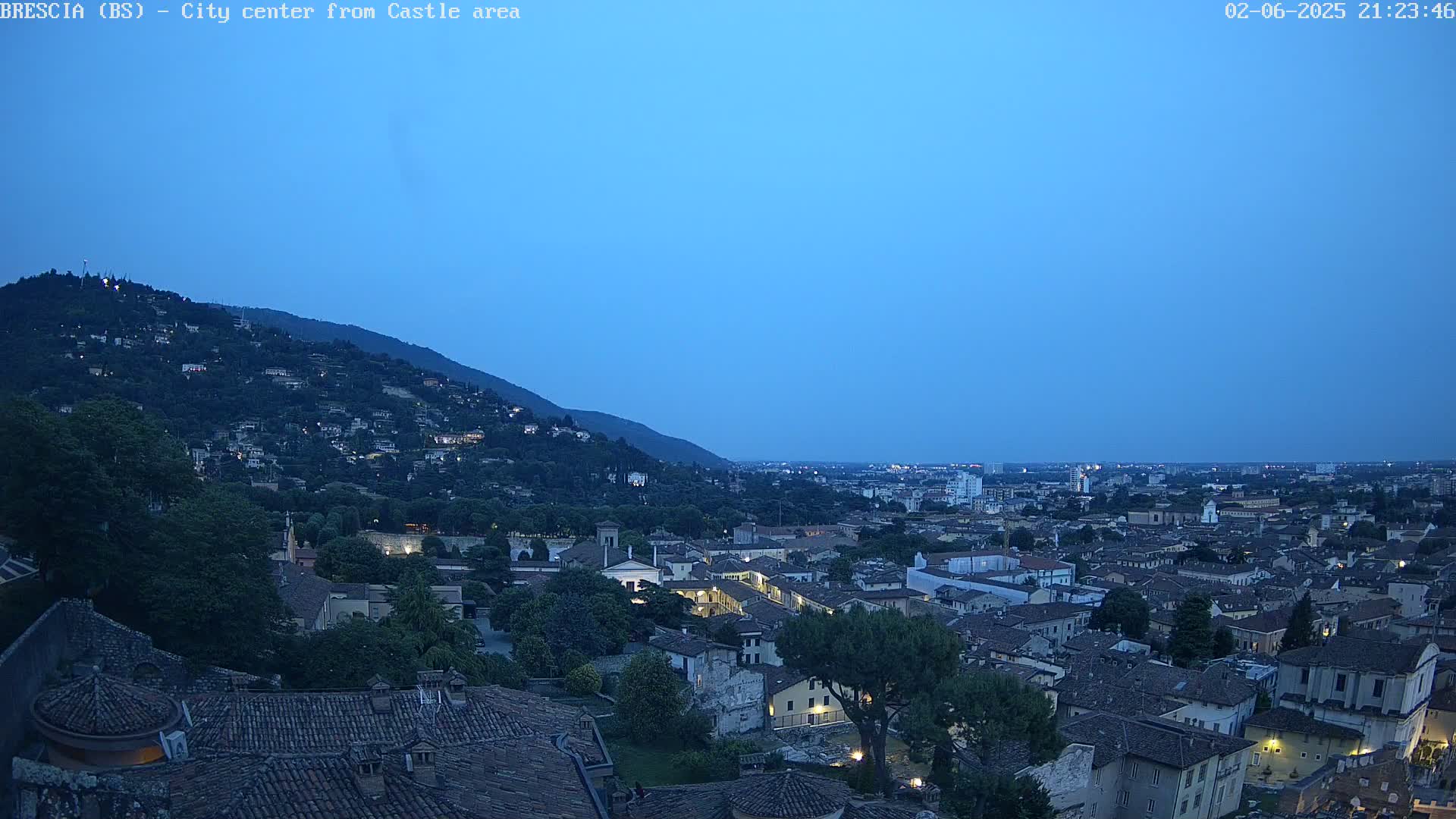 A nighttime view shows a city nestled against a hill, under a twilight sky.