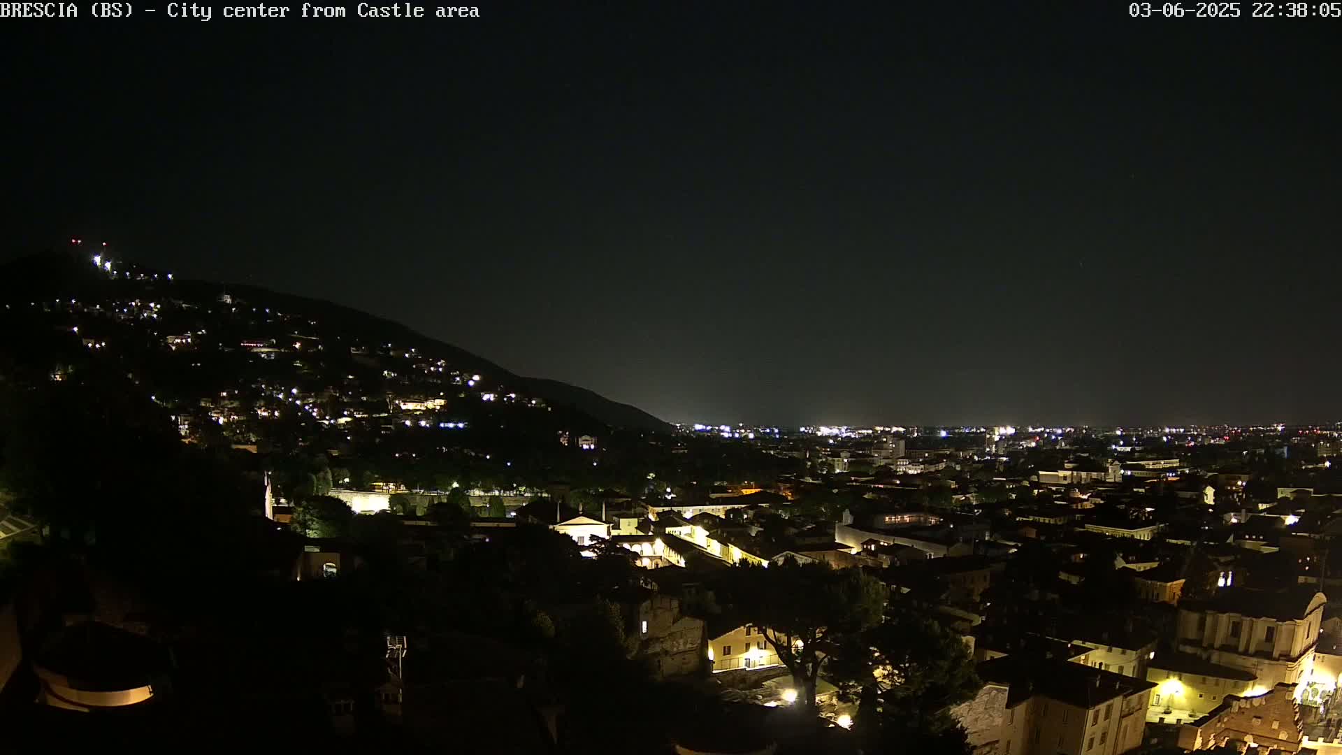 A nighttime view shows a city nestled against a hill, illuminated by scattered lights under a clear, dark sky.