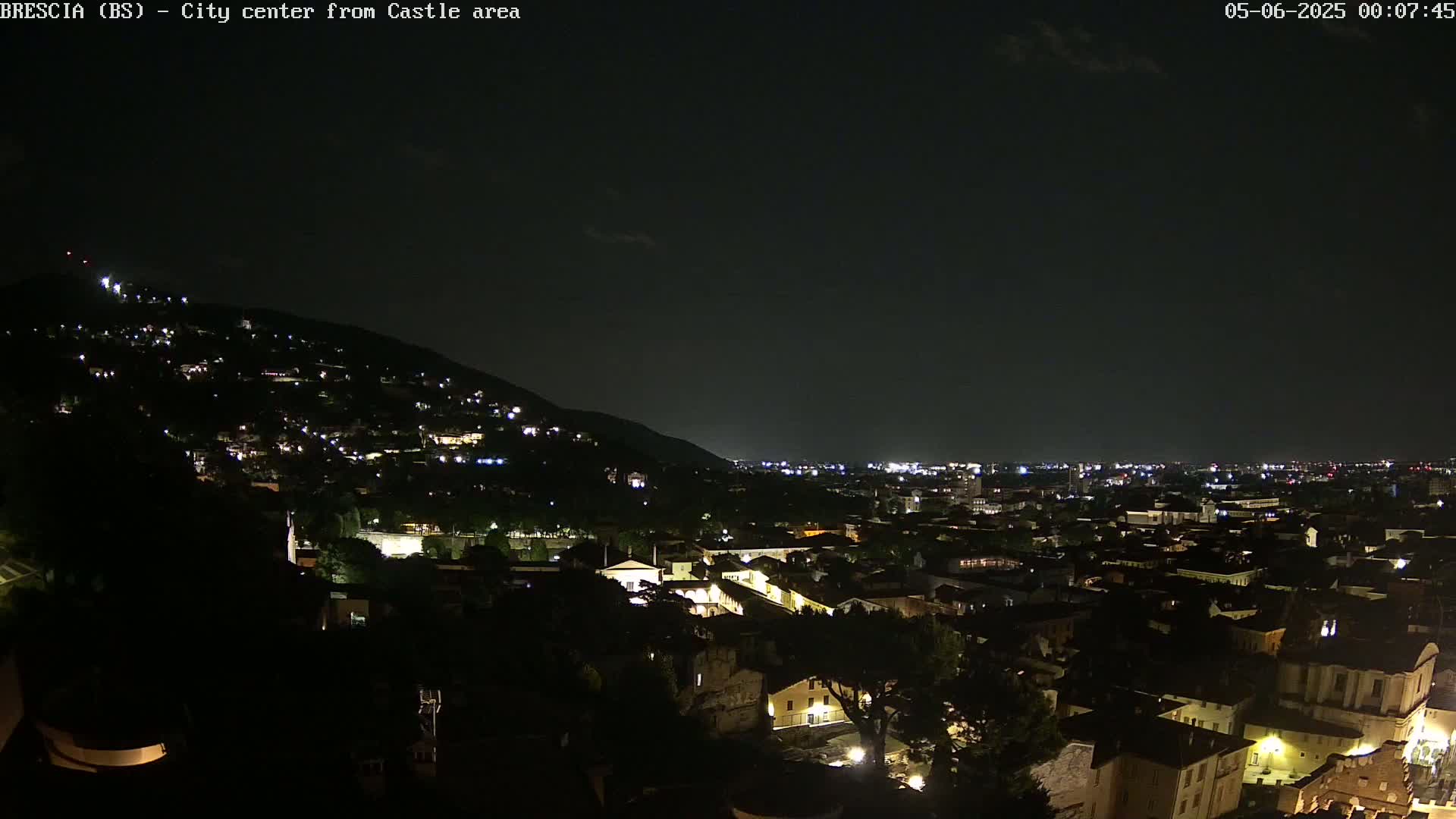 A nighttime view of a city nestled against a hill, illuminated by scattered lights under a dark sky.