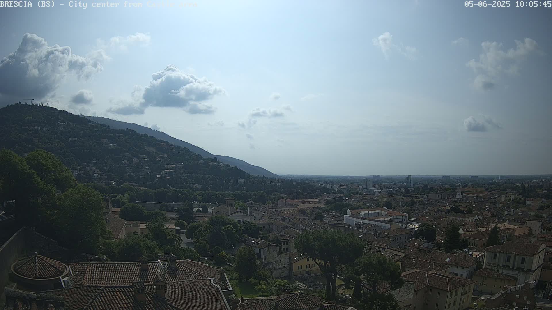 A partly cloudy day reveals a panoramic view of a city nestled against a hillside, with terracotta rooftops stretching to the horizon.